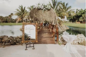 Bridge entrance with a floral arch and welcome mirror leading across the water