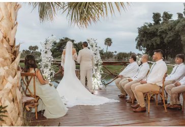 Wedding ceremony on the wooden deck at the water's edge with guests seated under palm trees