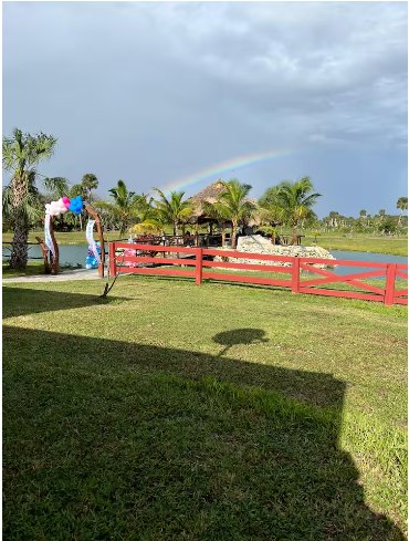 Rainbow over the property with red ranch fencing and open green pasture